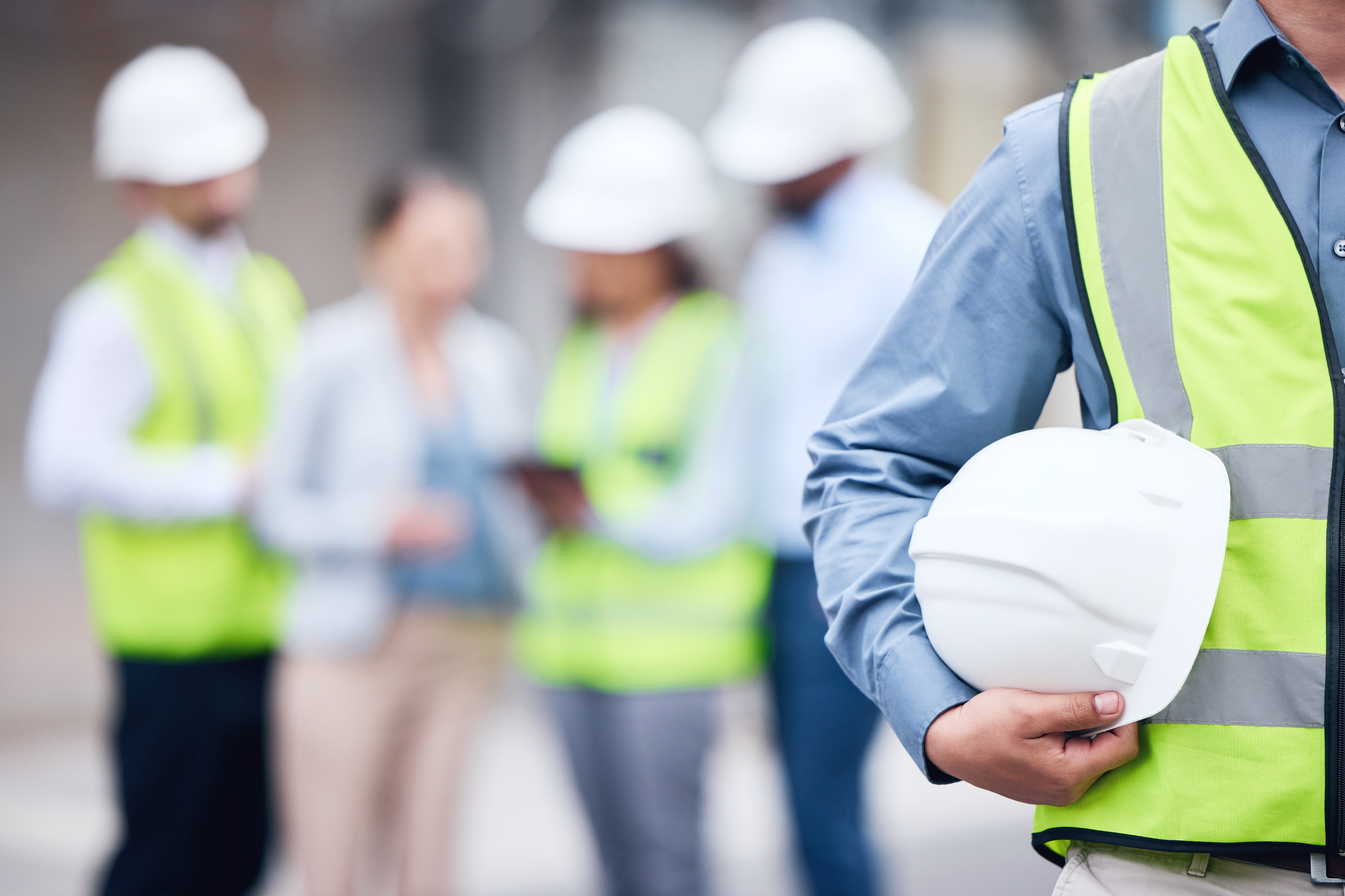 Person with hard hat under arm, wearing hi vis in front of group of people wearing hi vis